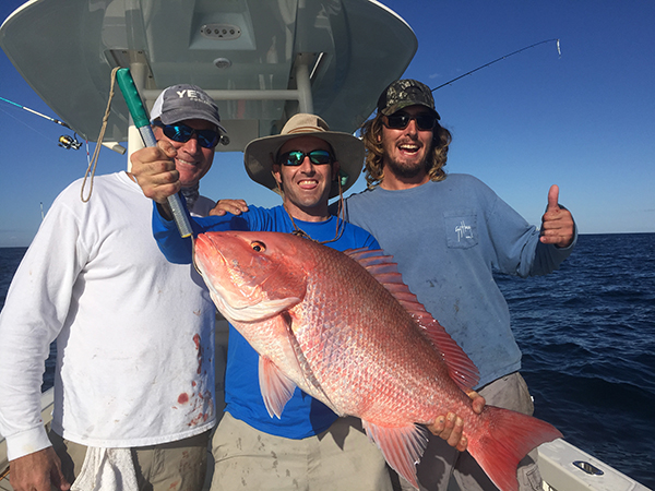 Three men holding a huge American red snapper while fishing on Hilton Head